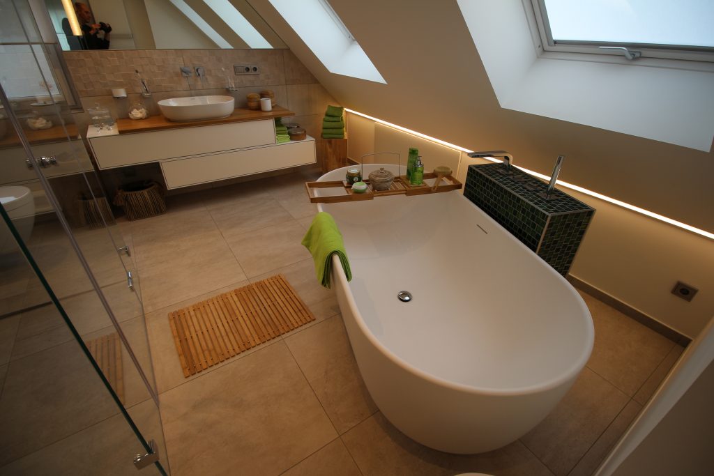 Freistehende ovale Badewanne mit indirektem Licht an der Wand im Hintergrund.