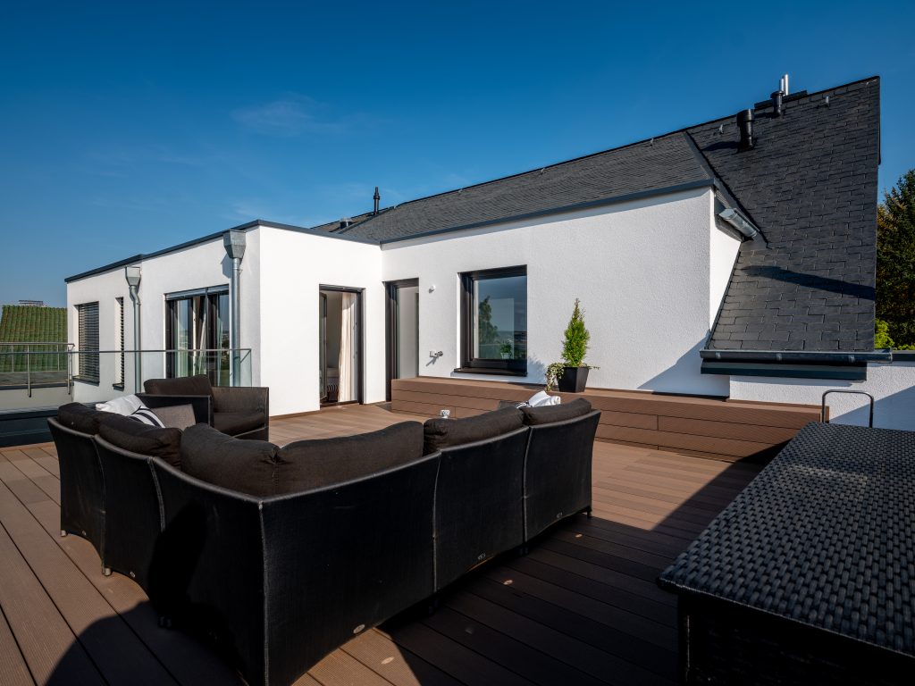 Moderne und gemütliche Dachterrasse, die mit einem Holzboden und einer Sitzgelegenheit sowie eine Sofalounge ausgestattet ist.