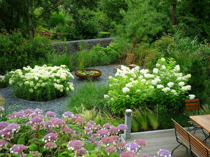 Botanisches Blumenbeet auf einem grauen Kiesbett mit Liegestühlen zur Entspannung.