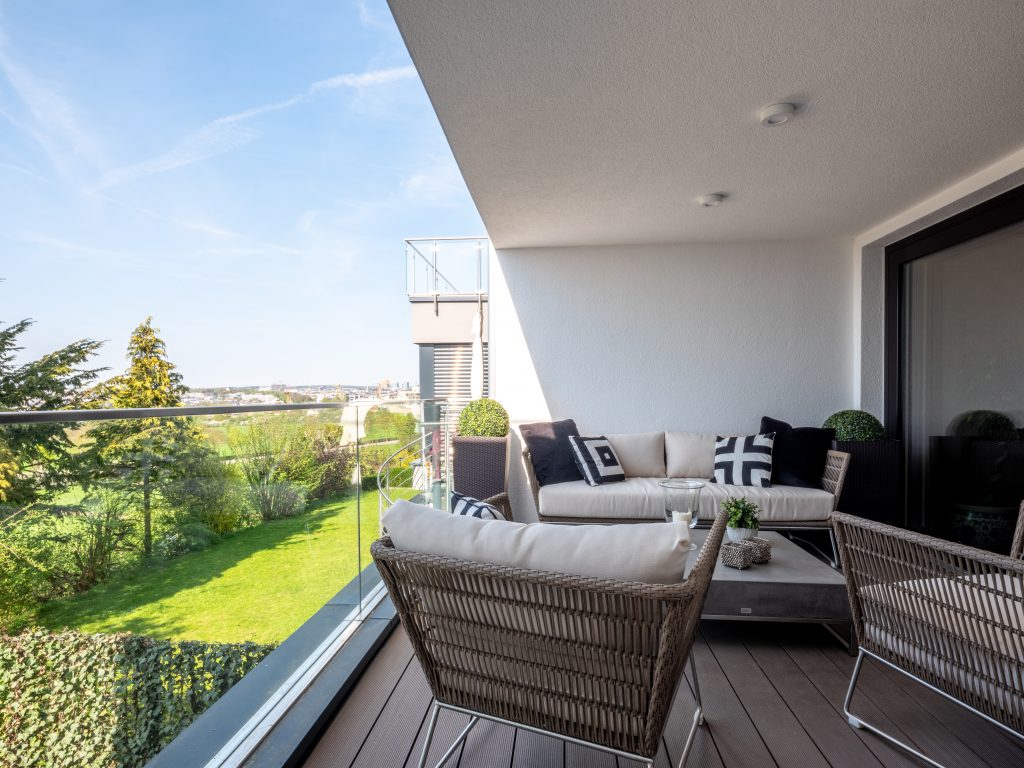 Überdachter Balkon mit gemütlichen Loungemöbeln und dunklem Holzboden.