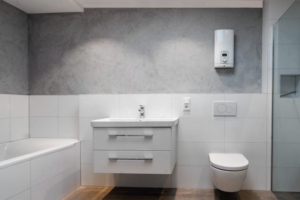 Modernes Badezimmer mit braunen Fliesen, bis zur Hälfte verlegte weiße Wandfliesen, weißer Badewanne, weißem Waschbecken mit Waschtisch und einem weißen WC.
