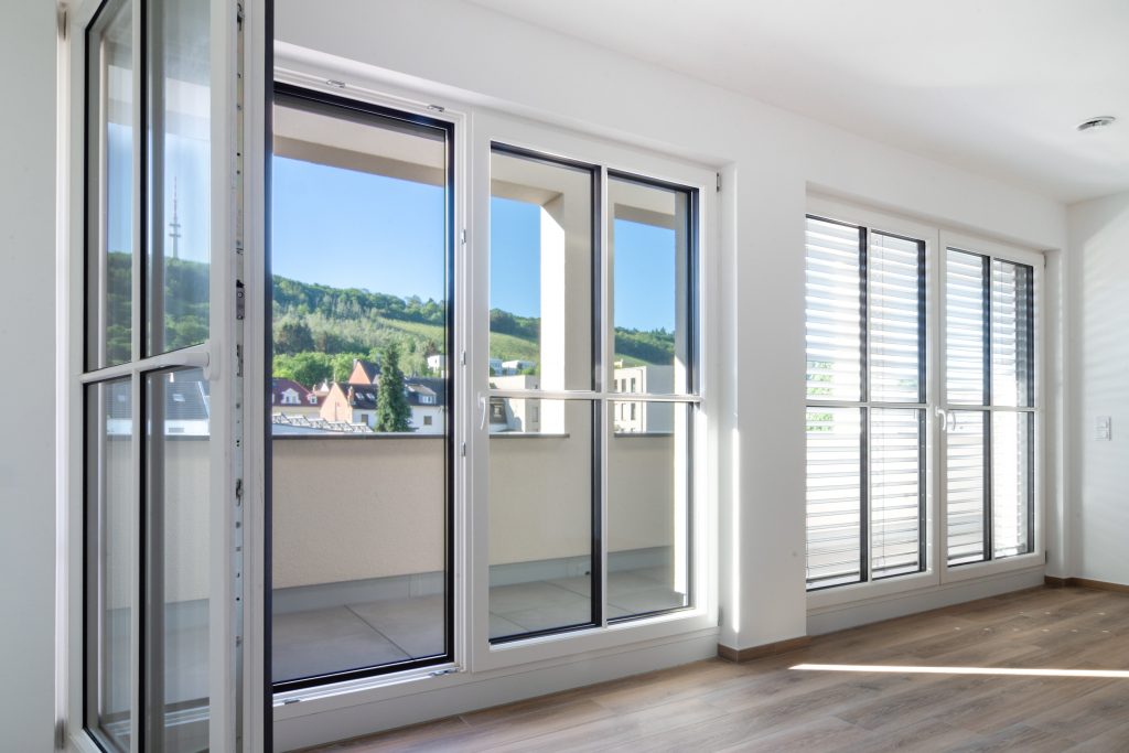 Mit Sprossen besetzte Fensterfront mit offener Balkontür in weiß und einem braunen Holzboden.