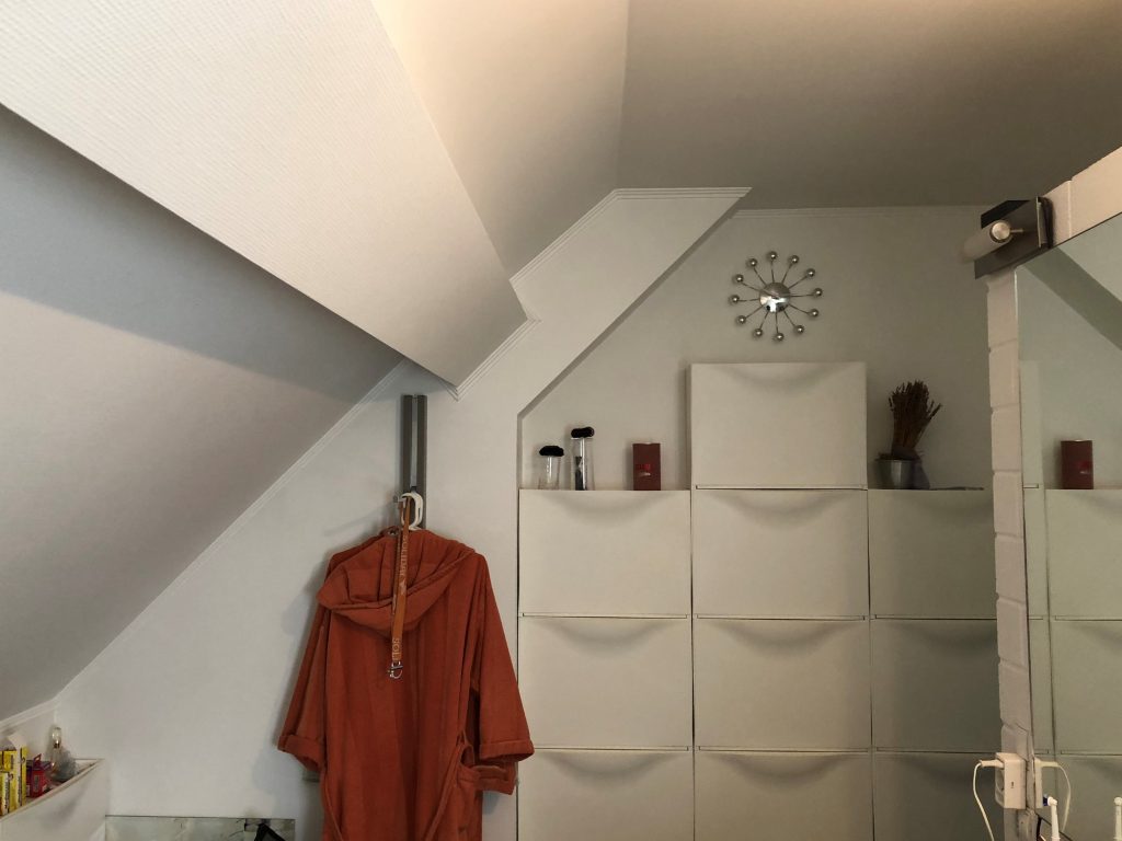 An einer weißen Wand im Dachgeschoss befinden sich viele weiße Schränke und ein orangener Bademantel.